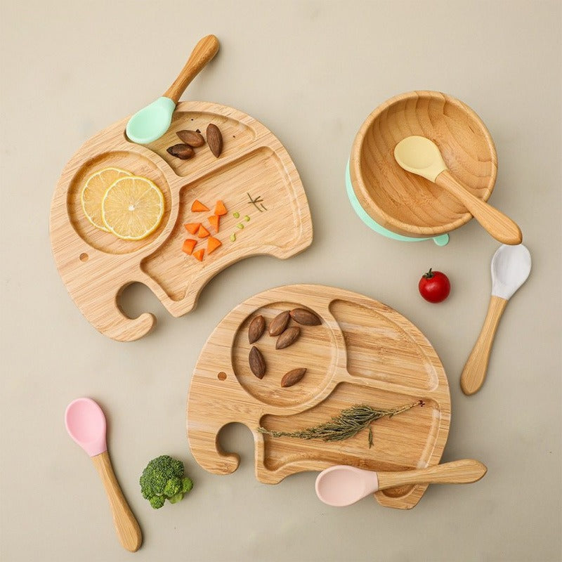 Wooden children's tableware set with plates, bowls, and utensils on a beige background
