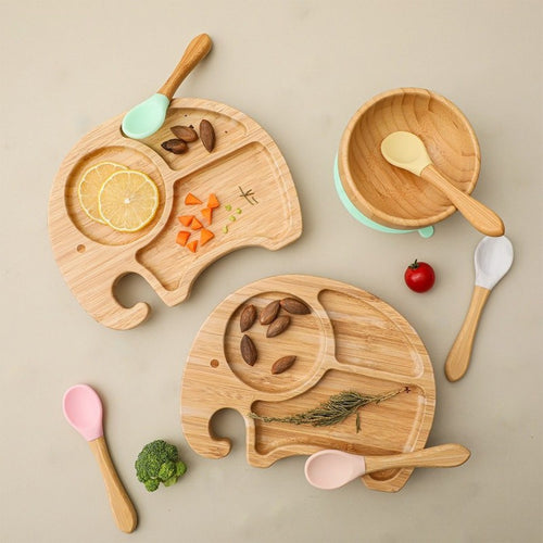 Wooden children's tableware set with plates, bowls, and utensils on a beige background