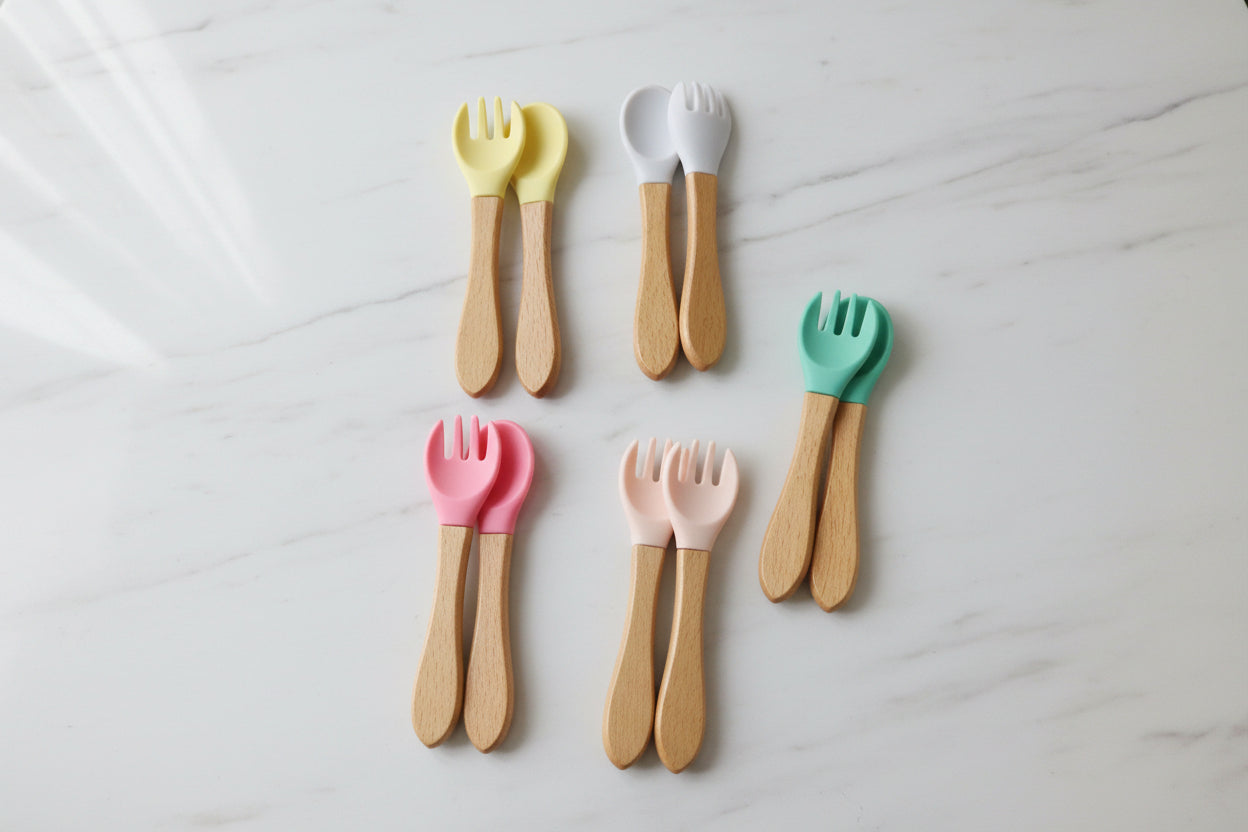 Set of wooden utensils with colored handles in clear packaging on a textured surface.